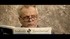 Photo of Aidan Quinn reading a newspaper